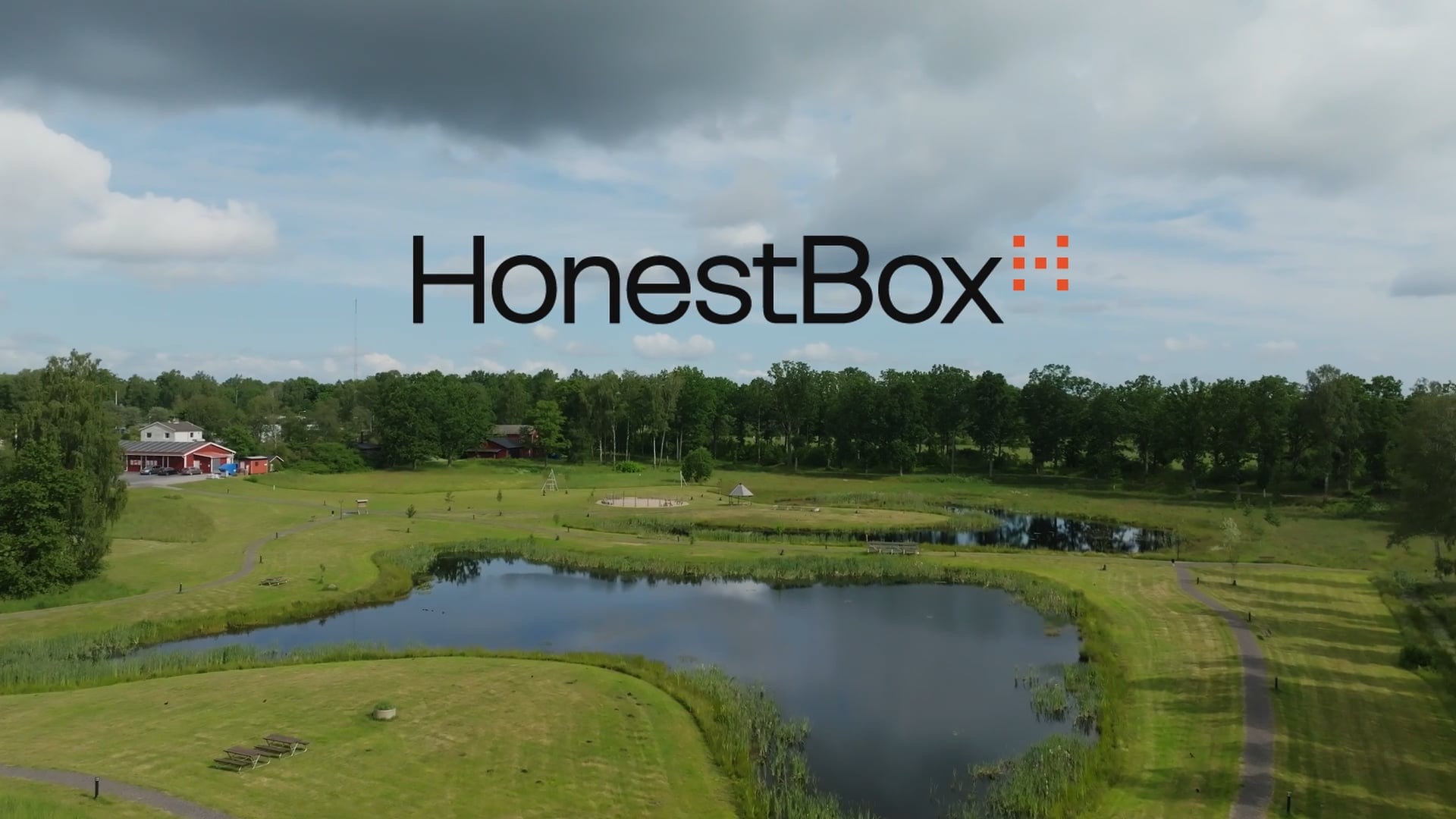 Drönarbild över ett grönt landskap med en sjö och röda hus, med HonestBox logotyp i bild.