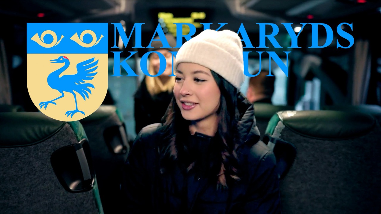 Still from the film: a young woman in a white beanie smiles on board the bus, with the Markaryd Municipality coat of arms and name in frame