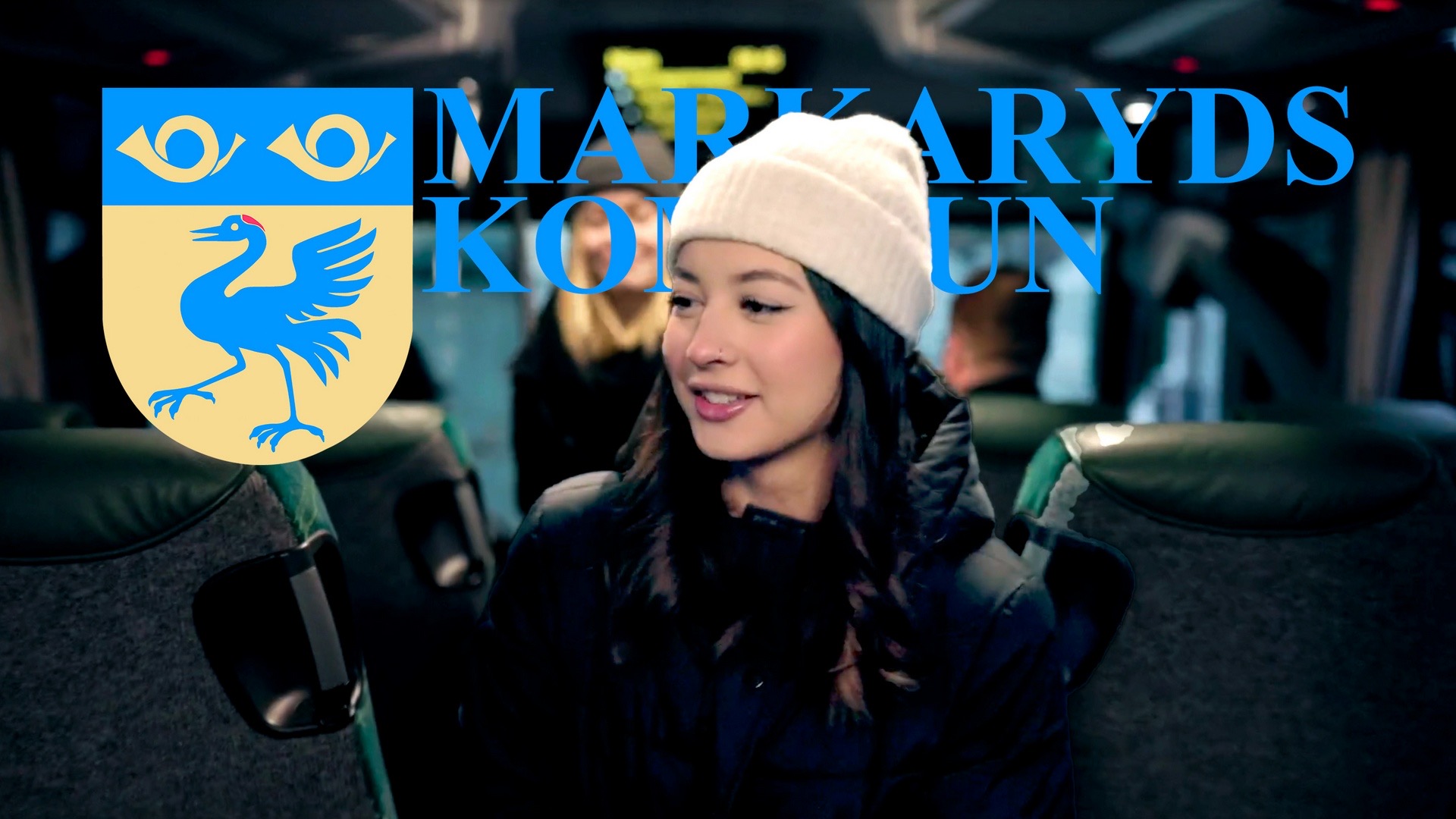 Stillbild ur filmen: en ung kvinna i vit mössa ler ombord på bussen, med Markaryds kommuns vapen och namn i bild.