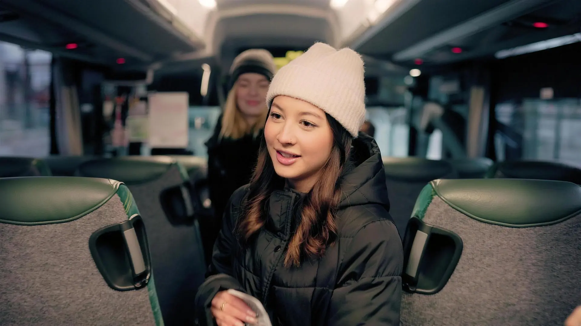 Stillbild ur filmen: en ung kvinna i vit mössa ler ombord på bussen.
