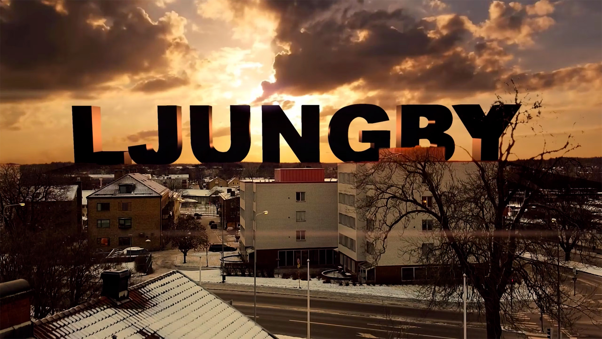 Stillbild ur timelapsefilmen: ordet LJUNGBY i stora bokstäver över stadens hustak i solnedgång, med snö på taken.