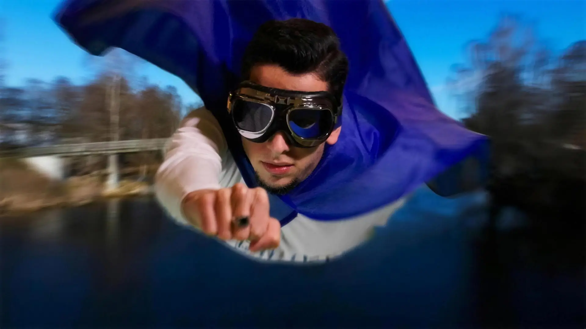 Stillbild ur Sjörikets rekryteringsfilm: en ung man i pilotglasögon och blå cape flyger över en sjö.