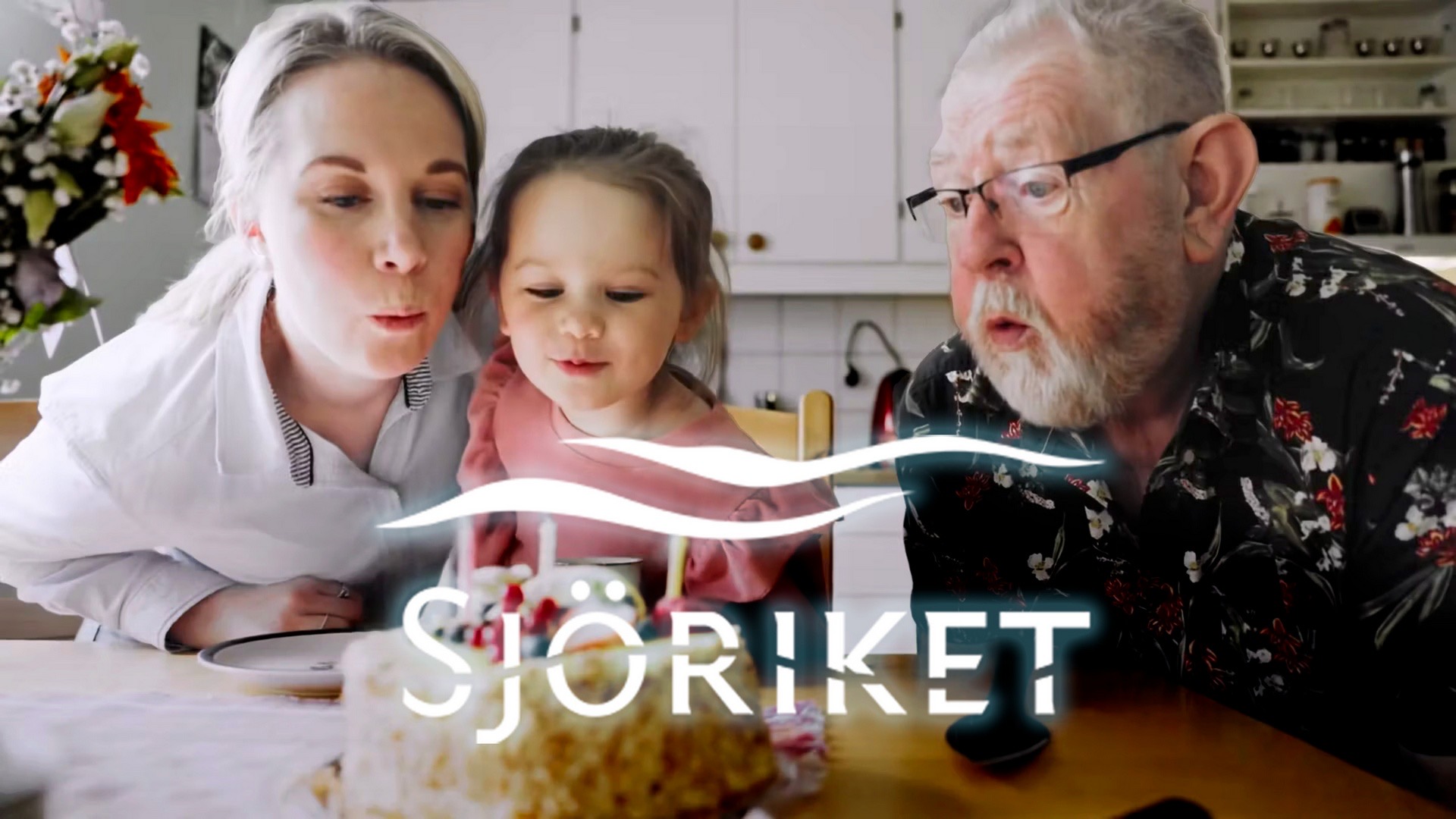 Stillbild ur Sjörikets reklamfilm: en kvinna, ett barn och en äldre man blåser ut ljusen på en tårta i ett kök, med Sjörikets logotyp i förgrunden.