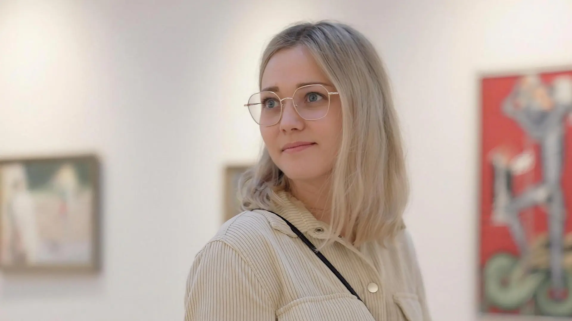 Stillbild ur kulturfilmen för Visit Ljungby: en ung kvinna i glasögon ser sig omkring i ett konstgalleri.
